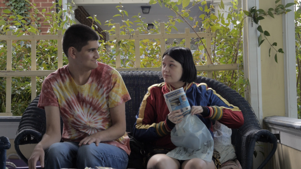 Two young adults, a male and female, sit on a couch folding newspapers