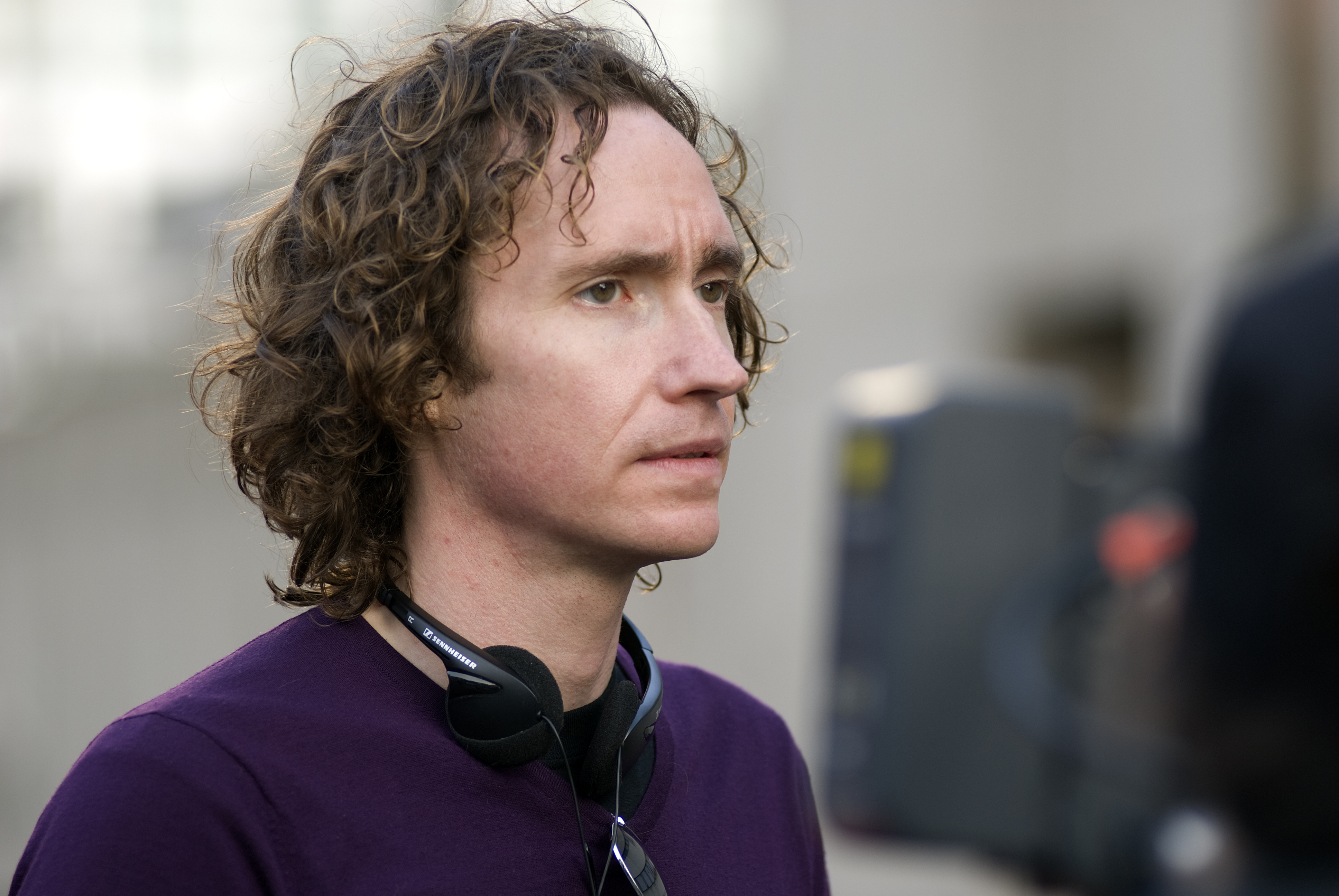 A man in a purple shirt and headphones resting on his neck looks to the right.