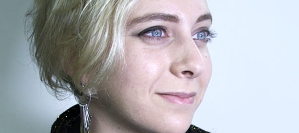 A woman with short, dirty blonde hair sweeping down to the side looks forward with a smile.