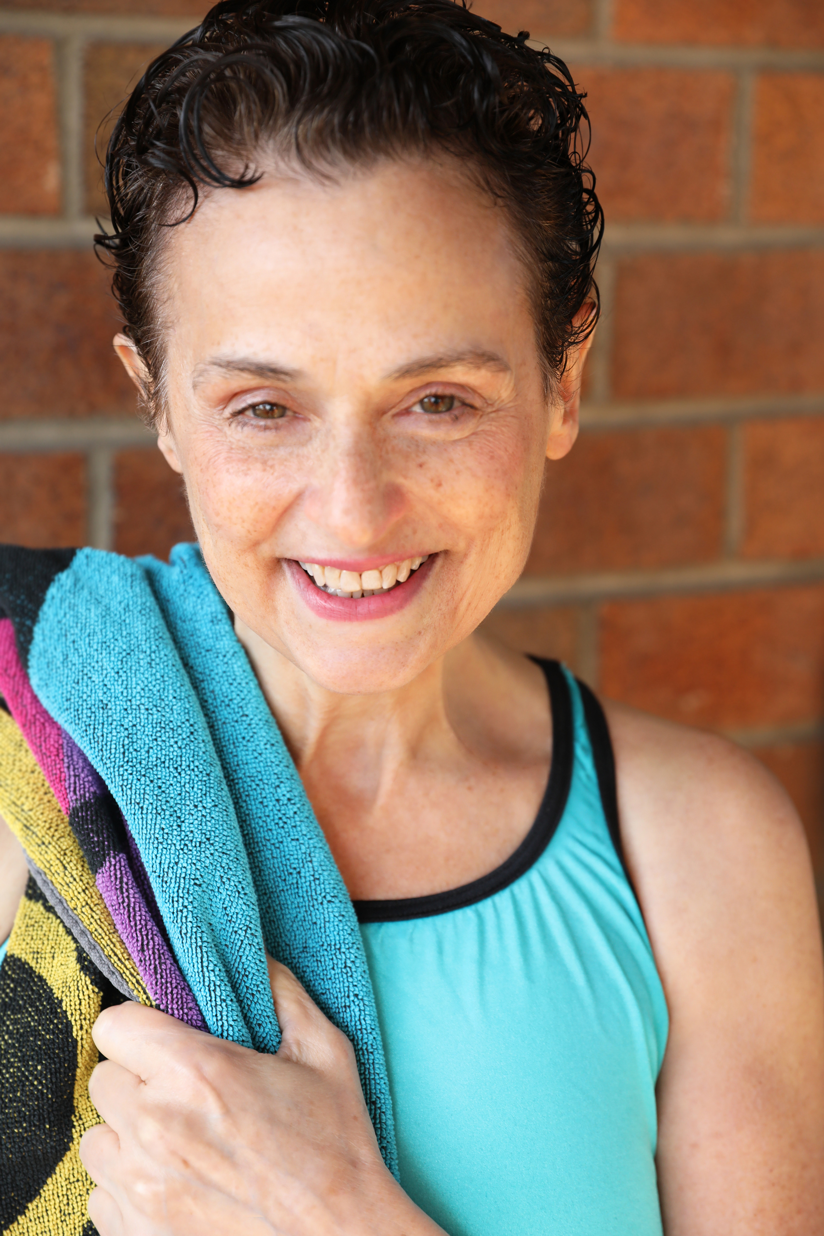 A short-cut haired woman wearing a light blue swimsuit, with a towel on her right sholder