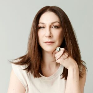 a woman with long brown hair, wearing a white shirt, leaning her chin on her left arm.