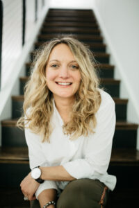 A picture of Megan Evans. A young woman with blond hair seating on a wooden stair case