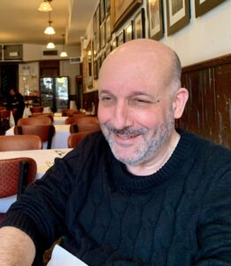 a bold man with a grey stubble, smiling looking down