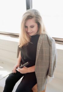 A young woman with blond long hair is looking down, holding a guiding cane