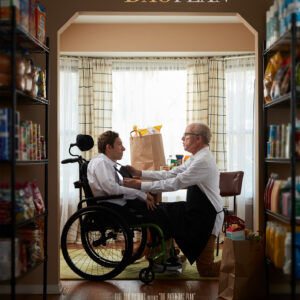 A movie poster for the film “The Paper Bag Plan” features a young man with dark hair in a wheelchair, wearing a white dress shirt. He is being assisted by an older man with glasses, who is dressed in a shirt and apron. They are surrounded by shelves filled with food and positioned in front of a window.