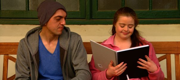 A man looks at a woman looking at a notebook on a bench