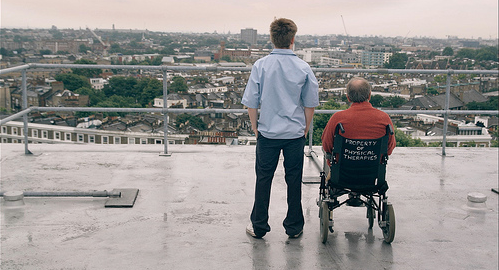 A man stands next to a man in a wheelchair on a roof