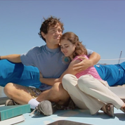 A teenage boy and teenage girl sit on the ground hugging