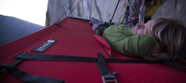A man lays back on a hanging tent on a cliffside