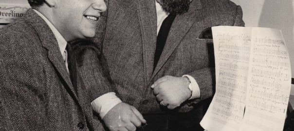 A black and white image of two men looking a music on a piano