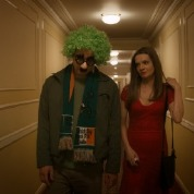 A man wearing costume glasses and a green wig walks with a woman in a red dress