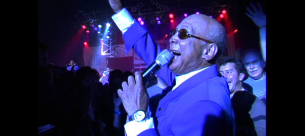 A man raises his hand while speaking into a microphone