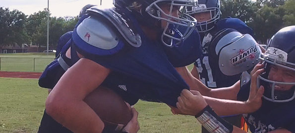 A man in a football uniform carrying a football runs into other football players