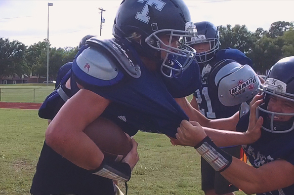 A man in a football uniform carrying a football runs into other football players