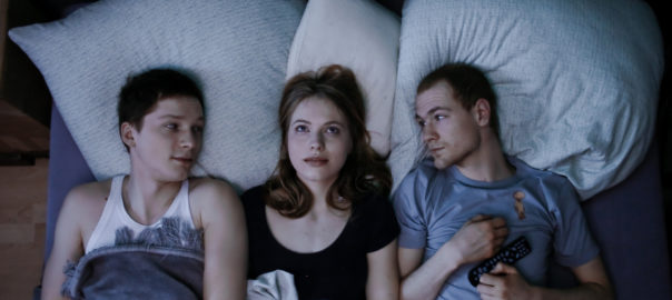 A woman lies between two men in bed