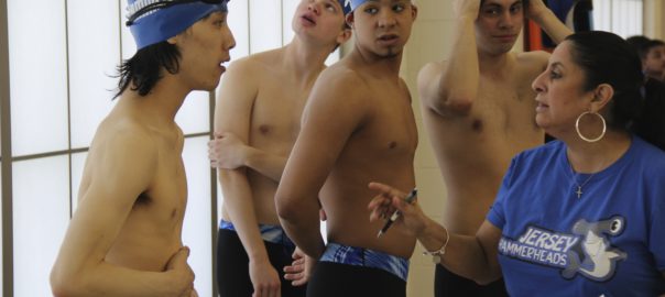 A group of swimmers stand next to a woman with a clipboard