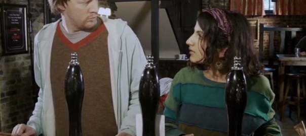 A man and a woman look at each other in front of beer taps at a bar.