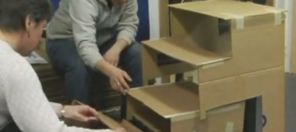 Two people construct a structure out of cardboard boxes