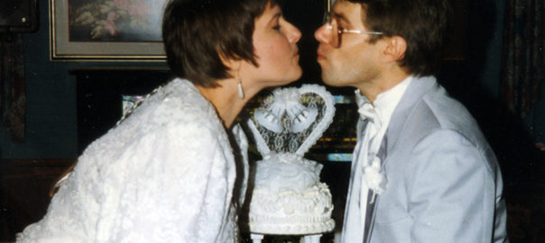 A man and a woman kiss over a wedding cake