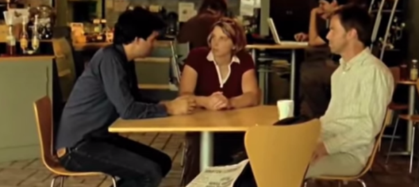 Three people sit at a wood table talking in a cafe