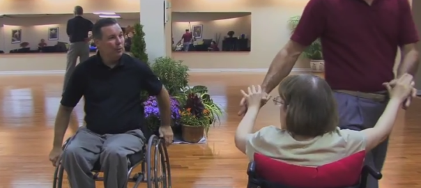 A man in a wheelchair looks at a woman in a wheelchair who is dancing