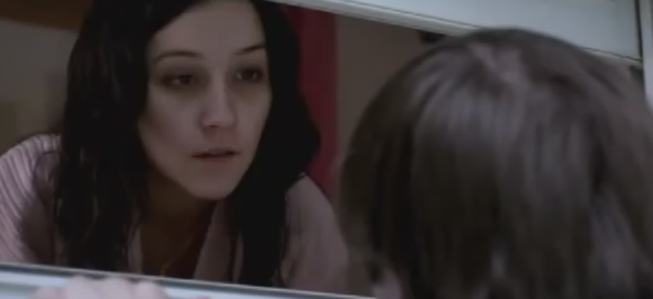 A woman looks through a cracked window at another person