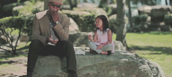 A man sits on a large rock with a young girl in a park