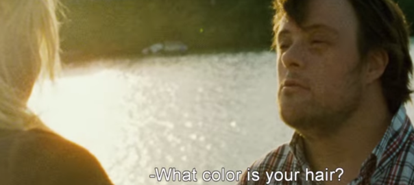 A man speaks to a person in front of him. There is a lake behind him.