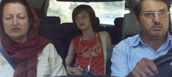 A man and a woman are in the front seats of a car that is driving. A boy sits in the back of the car.