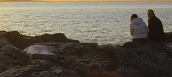 A couple sits on rocks above the ocean
