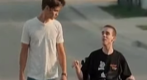 Two men travel down the street. One is in a wheelchair