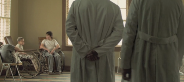 Two doctors stand in front of a room with patients sitting in chairs