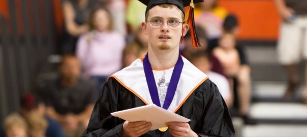 A man in graduation cap and gown holds a piece of paper
