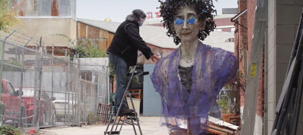 A person stands next to a large sculpture of a person