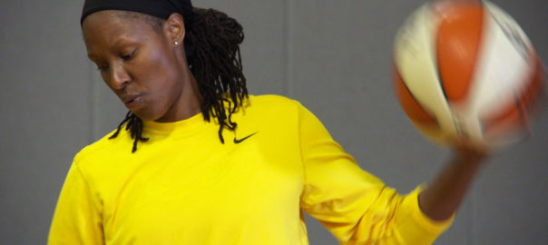 A woman in a bright yellow shirt holds a basketball