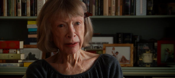 A woman talks to the camera with books behind her