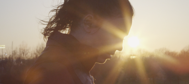 A woman with a ponytail looks down as the sun sets behind her.