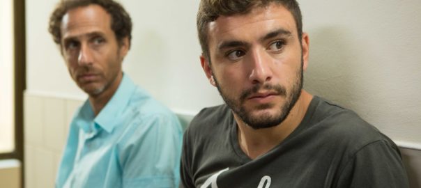 A teenage boy and a man sit and look to the right