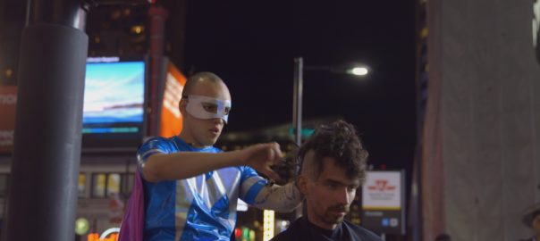 A man dressed as a superhero cuts a man's hair