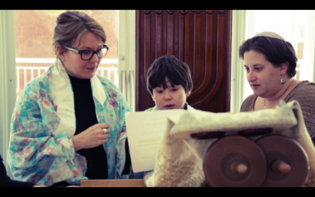 A boy stands with two women next to him. There is a torah in front of them.