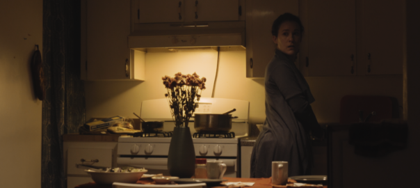 A woman stands in a kitchen. A bouquet of flowers is on a table
