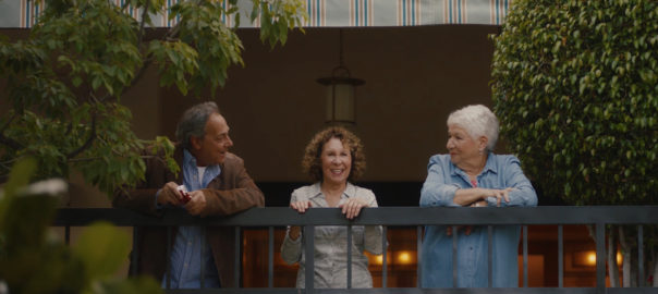 A man and two women lean over a balcony talking