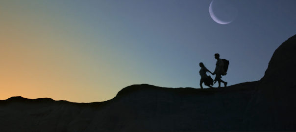 Two people cross a ridge at twilight