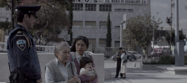 Two women sit on a bench with a baby. A police officer stands next to them