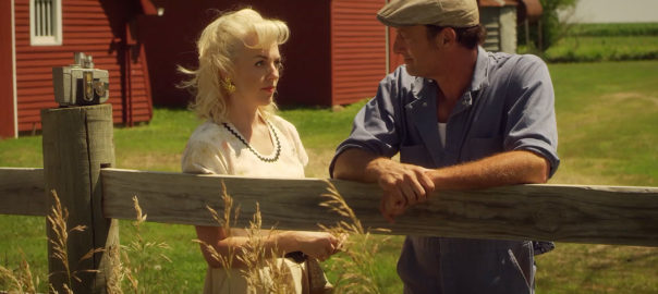 A man and women talk in a field in front of a wood fence