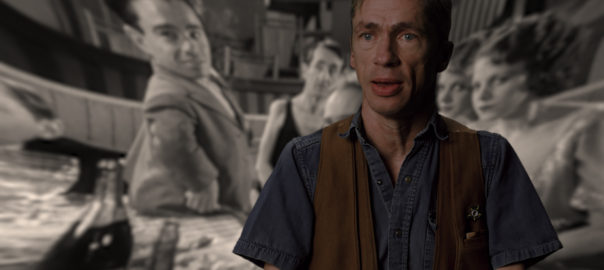 A man sits in front of a projected black and white image