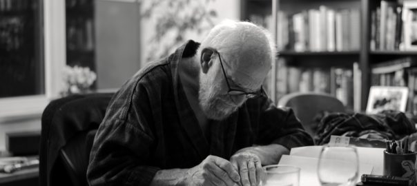 Oliver Sacks leans over his desk writing. The image is black and white.