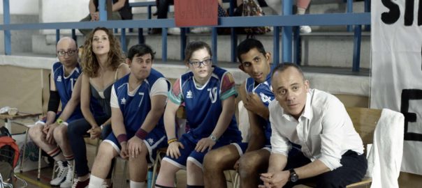 A group of basketball players in blue uniforms sit on a bench next to their coach.