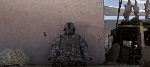 A man who is an amputee leans against a while dressed in a military uniform