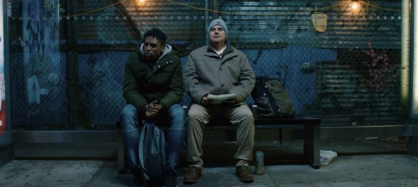A young man sits on a bench next to a man .